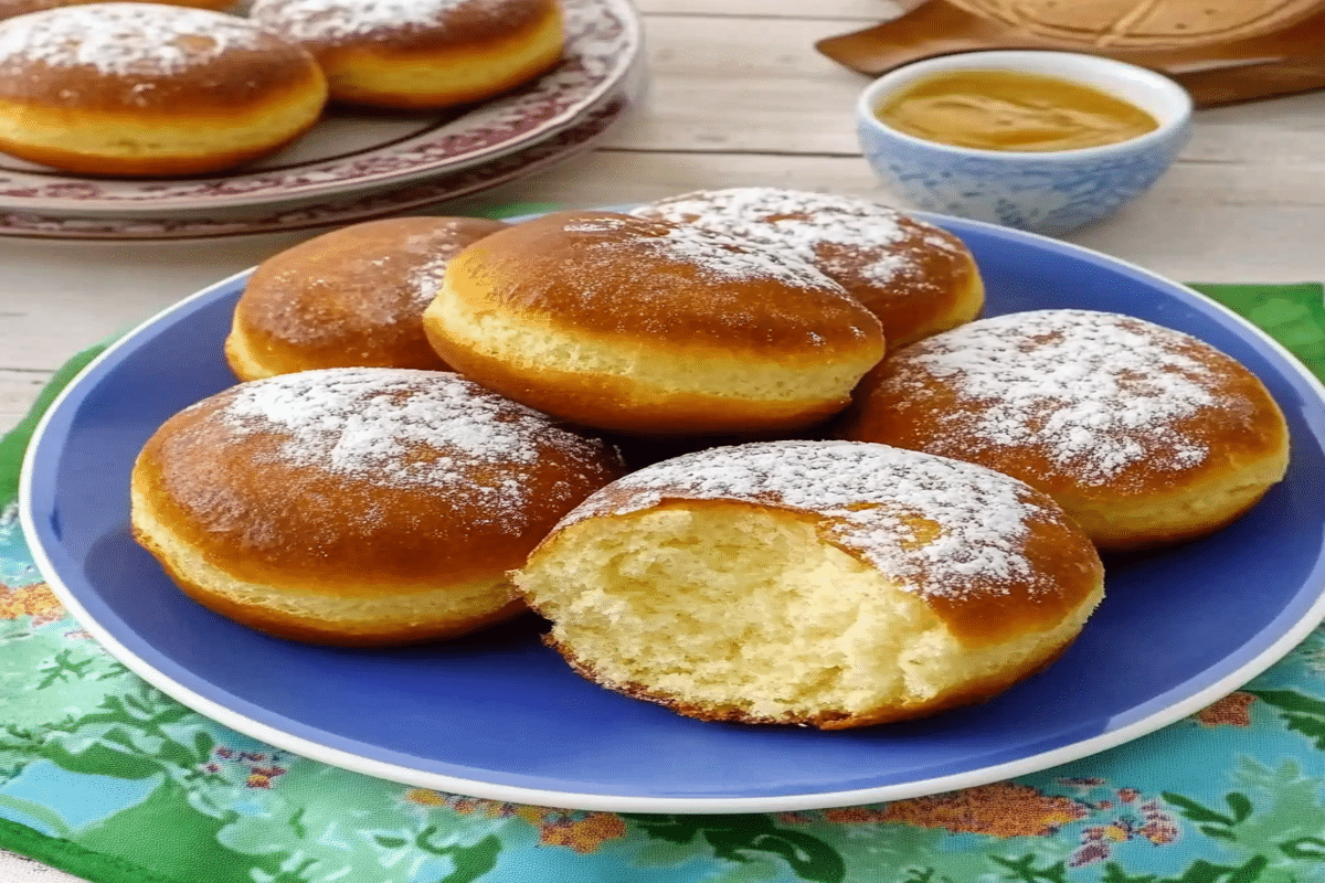 Secrete pentru gogoși pufoase prezentate în prim-plan, gogoși aurii pudrate cu zahăr pe o farfurie albastră.