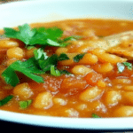 Fasole prajita in sos de rosii, garnisita cu patrunjel verde in bol alb