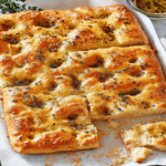 Focaccia reteta italiană – cum iese moale și aerată 6 focaccia reteta în prim-plan, cu alveole umplute cu ulei și ierburi aromate