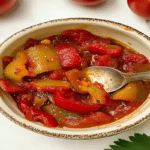 Ardei copți la airfryer în 12 minute – rețeta ușoară pentru ardei copți perfecți 6 Ardei copți la airfryer serviți într-un bol mic cu lingură, în sos de roșii cu ardei roșii și galbeni